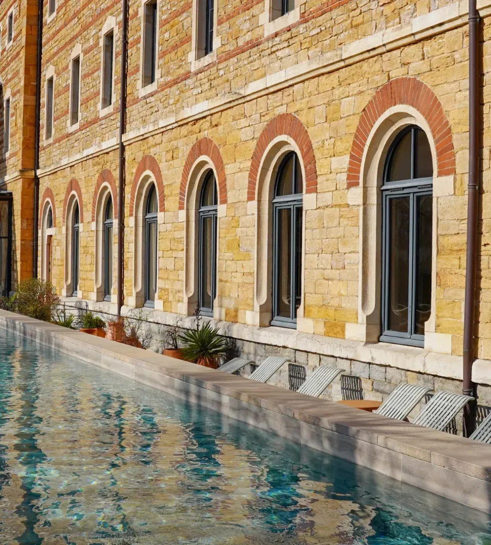 Piscine longue devant bâtiment en pierre.